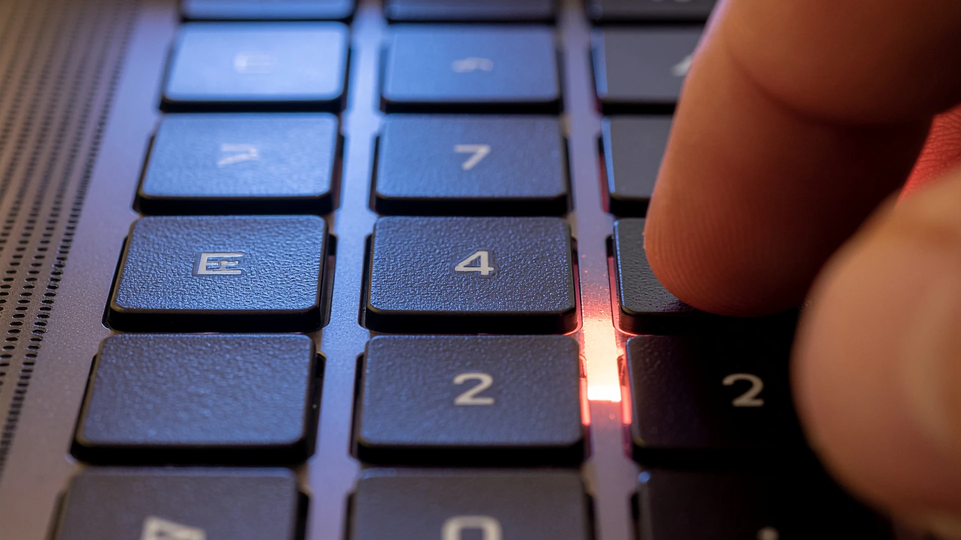 Finger pressing a key on an illuminated keyboard